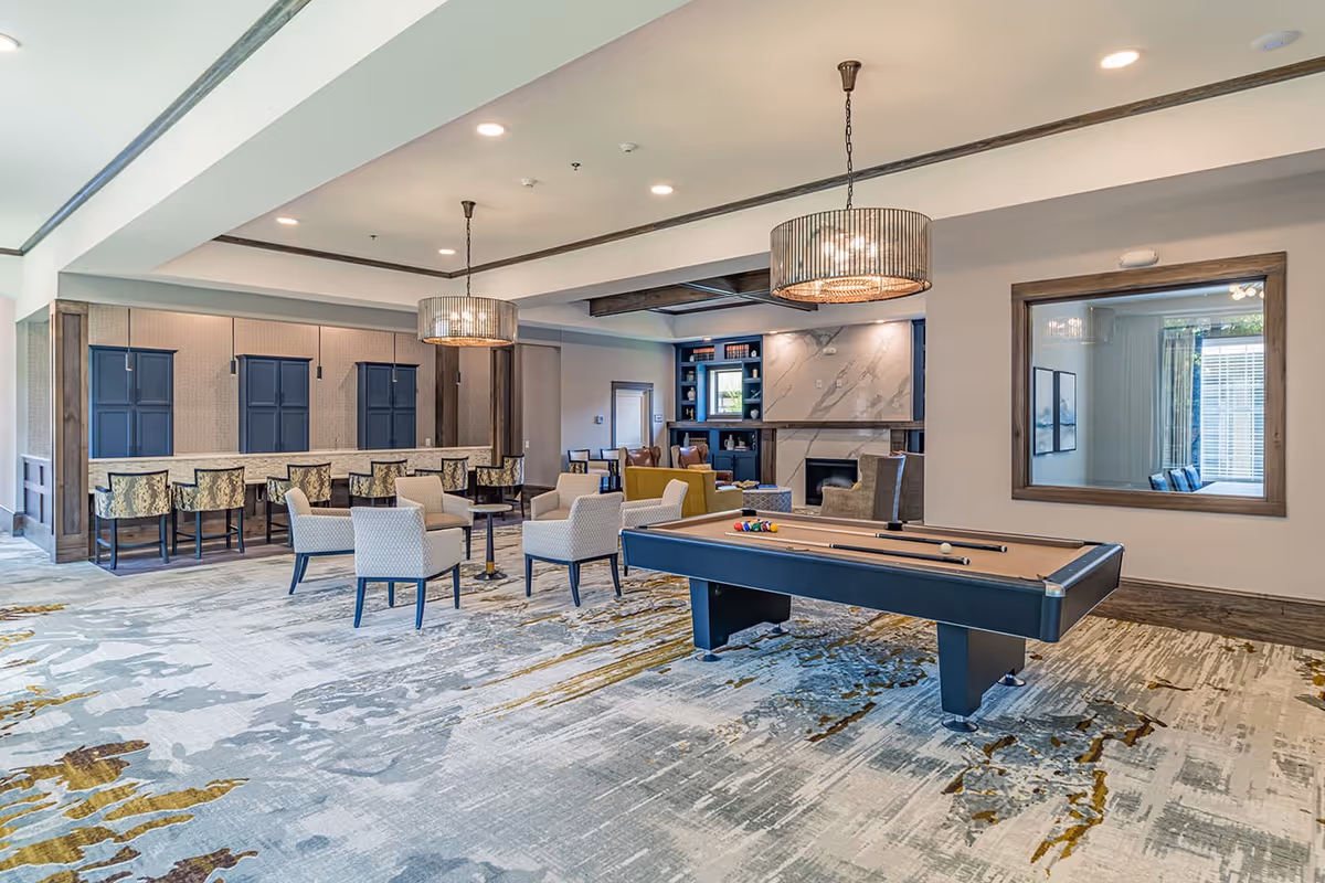 Spacious communal lounge with a pool table, multiple seating areas, and a bar counter under pendant lights.