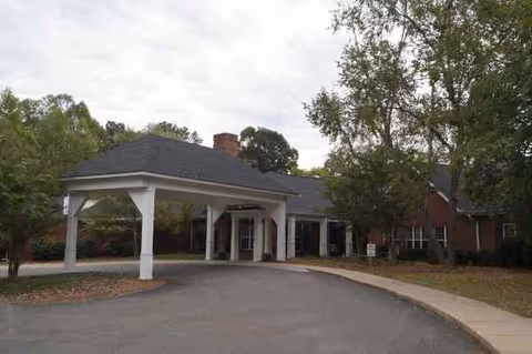 Exterior view of a senior living facility with a covered entrance and surrounding trees.