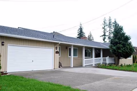 Single-story beige facility with white front porch, two-car garage, and green lawn.