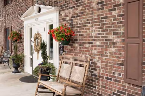 Exterior brick entrance with wreath, hanging flower baskets, and a wooden bench.