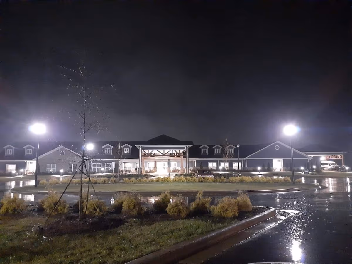 Nighttime view of a long, single-story nursing facility building lit by streetlights with a circular driveway and wet pavement.