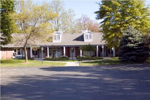 Front exterior of Georgetown and Cambridge Assisted Living building with trees and a parking lot.
