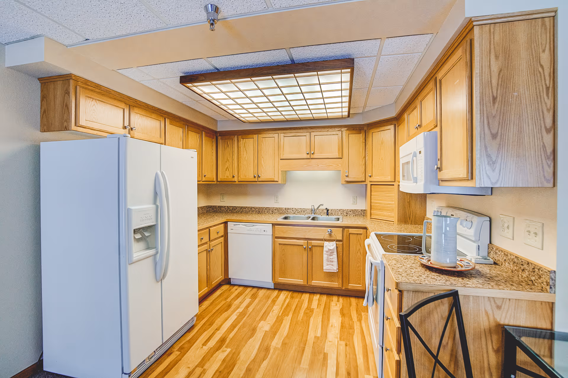 Well-lit kitchen with oak cabinets, white appliances (refrigerator, dishwasher, stove, microwave), granite-look countertops and wood flooring.