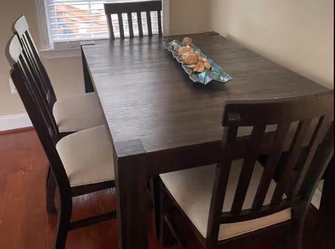 Dark wooden dining table with four chairs near a window in a bright dining area