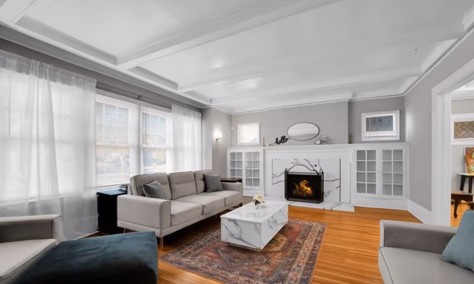 Bright living room with gray sofas, marble coffee table, fireplace, and large windows.