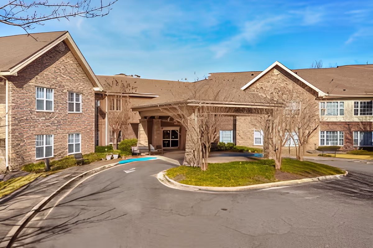 Front entrance of a two-story brick senior living facility with a covered porte-cochere and circular driveway.