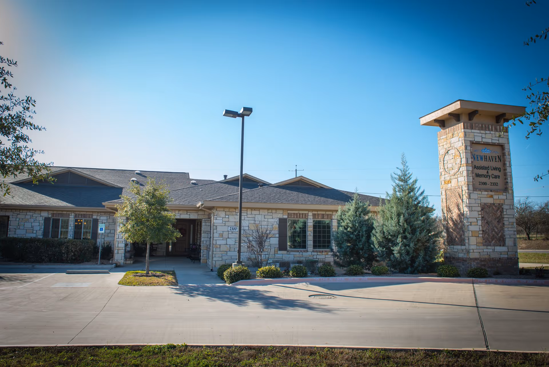 Stone-faced assisted living building front with entrance, landscaping, parking area, and a tall sign reading 'New Haven Assisted Living Memory Care'.