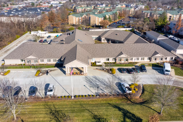 Aerial view of the single-story Cedar Creek of Bloomington Memory Care building with entrance canopy, parking lot, and surrounding lawn.