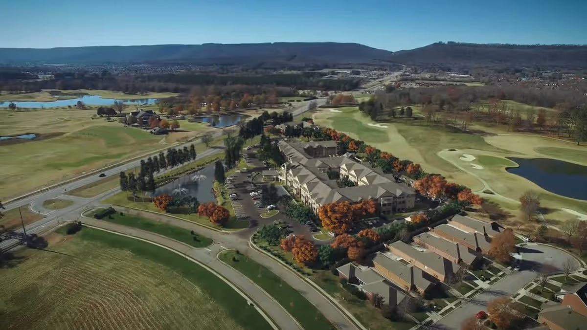 Aerial view of the Residences at Wellpoint facility surrounded by landscaped grounds, parking areas, and adjacent golf course with ponds and fairways, set against a backdrop of distant hills under a clear sky.