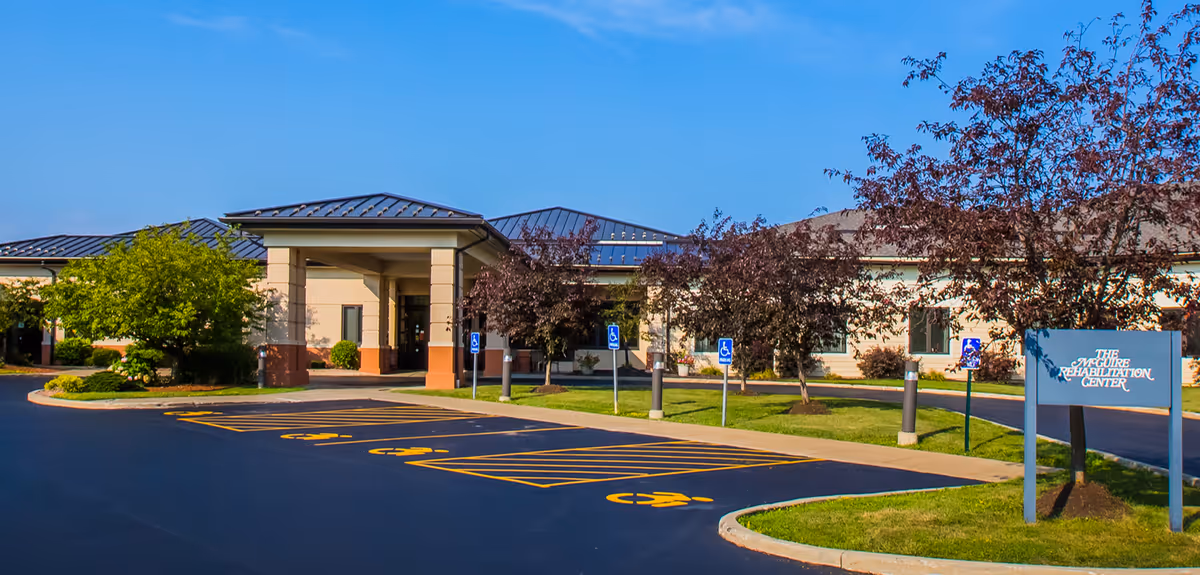 Front exterior of a single-story health care/rehabilitation facility with a covered entrance, accessible parking spaces, landscaping, and a sign.