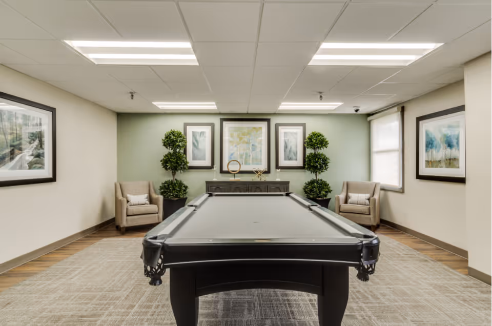 Pool table center stage in a furnished recreation room with chairs and art