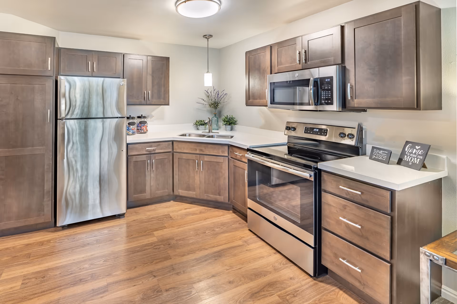 Modern kitchen with stainless steel refrigerator, stove and microwave, wooden cabinets, white countertops and hardwood floor.
