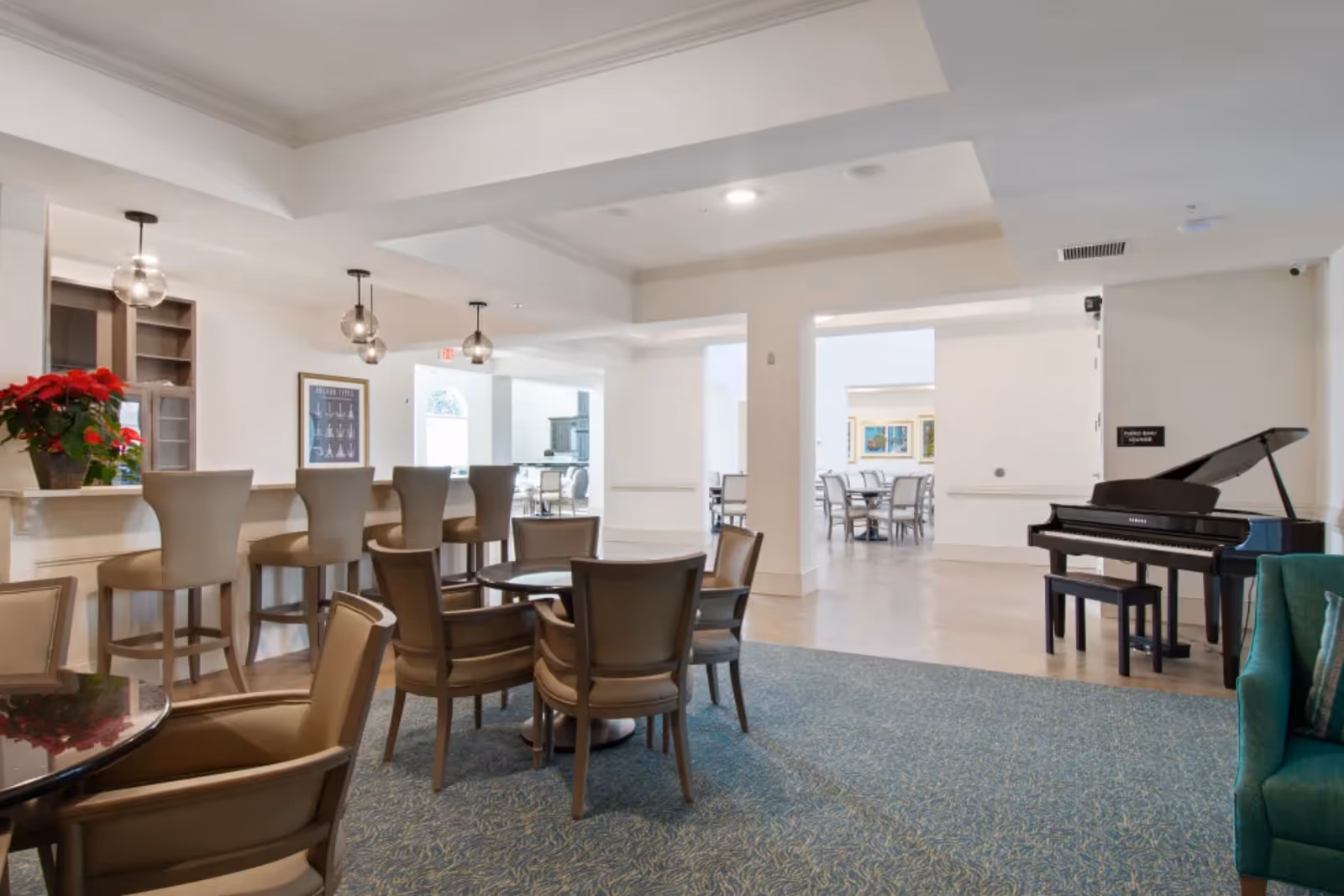Bright communal lounge and dining area with bar seating, round tables and a grand piano.