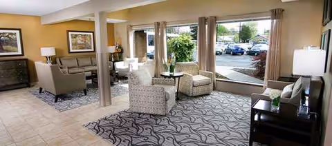 Spacious lounge area with seating, tables, lamps, and large windows overlooking parking lot.