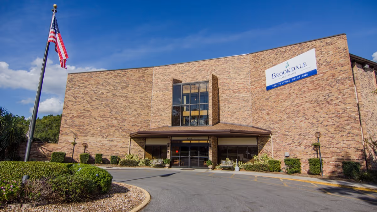Brick facade and main entrance of the Brookdale Lake Tavares senior living building with an American flag and curved driveway.