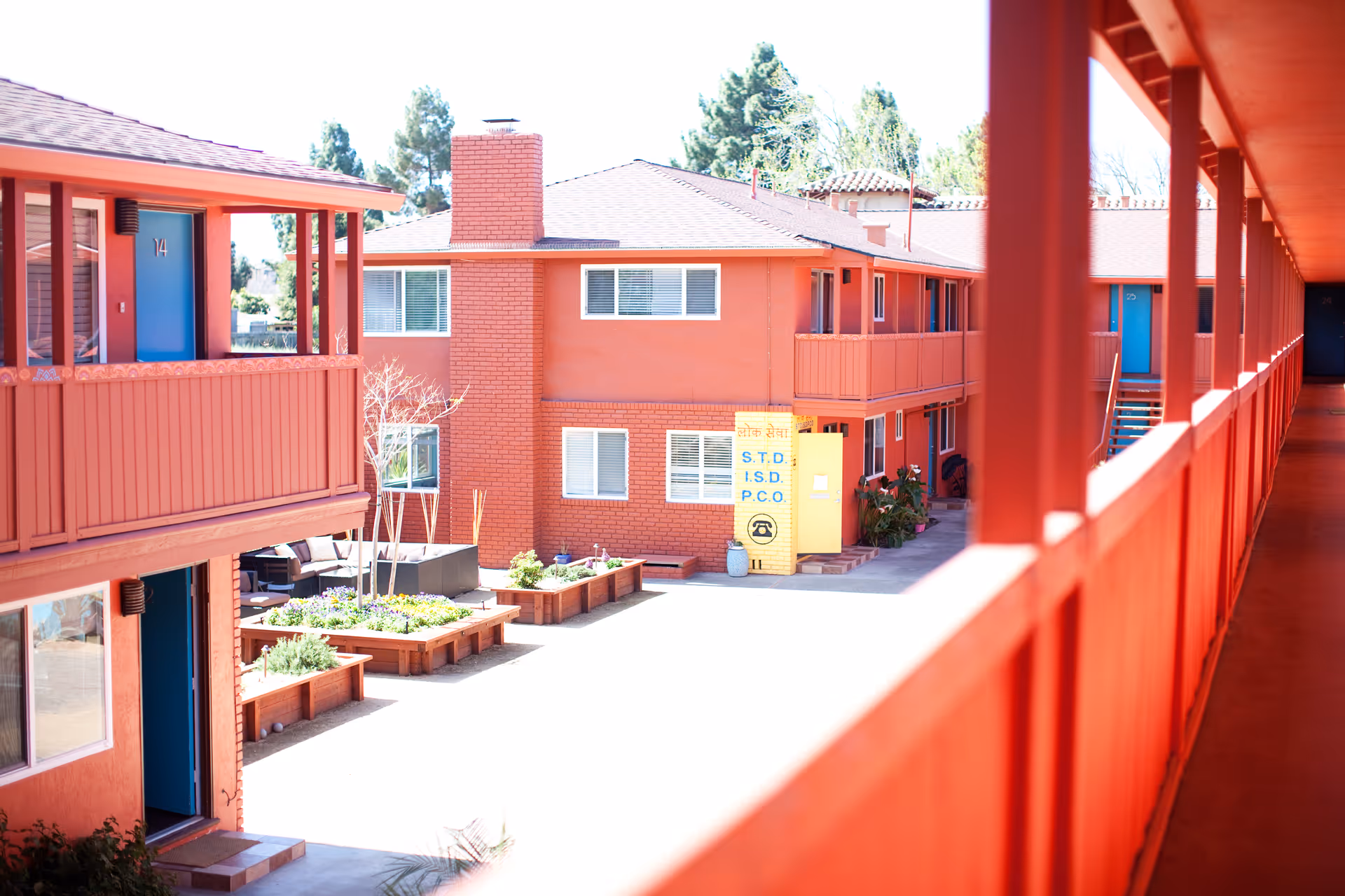 View of a bright coral-painted two-story courtyard and exterior walkway with blue doors and planter boxes.