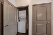 A small interior hallway closet with a stacked white washer and dryer between two closed beige doors.