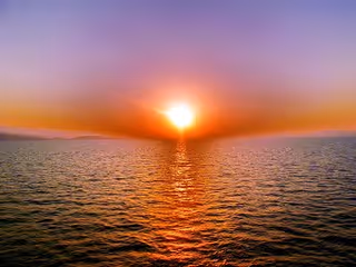 Vibrant sunset over open water with the sun low on the horizon and an orange reflection on the sea.