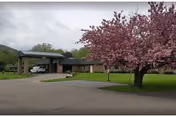 Front exterior of a single-story brick building with a covered driveway and a pink flowering tree on the lawn.