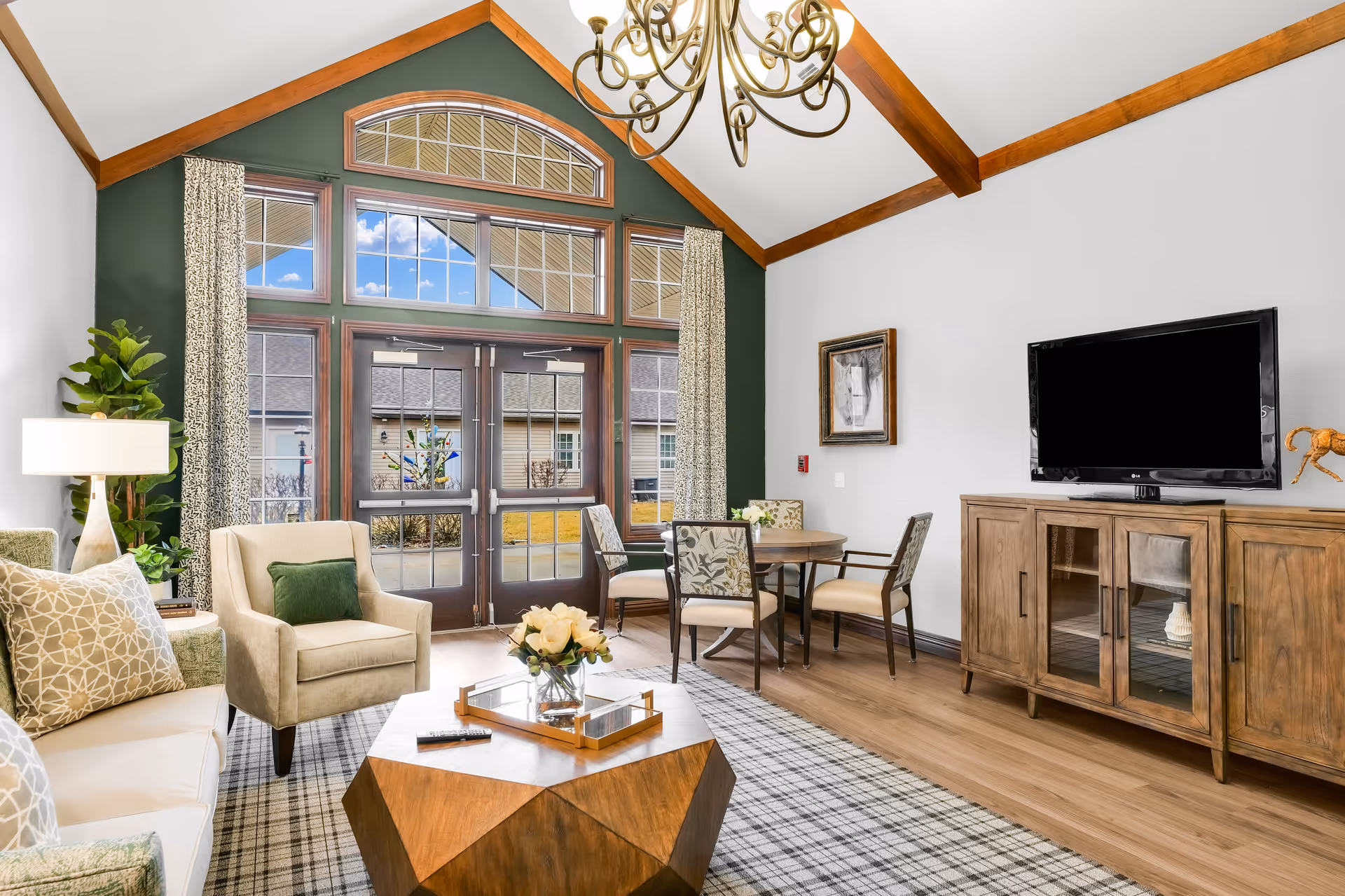 Bright common living room with seating, a wooden coffee table, a flat-screen TV, and tall arched windows and doors.