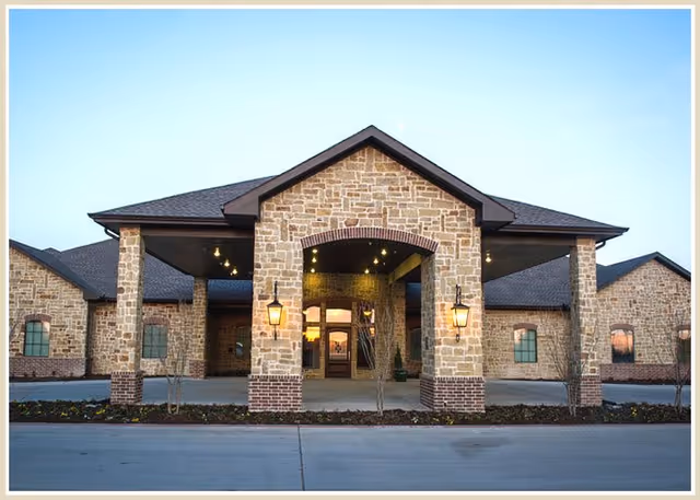 Front exterior view of a single-story building with stone and brick facade, featuring a covered entrance with two lantern-style lights and a paved driveway in front.