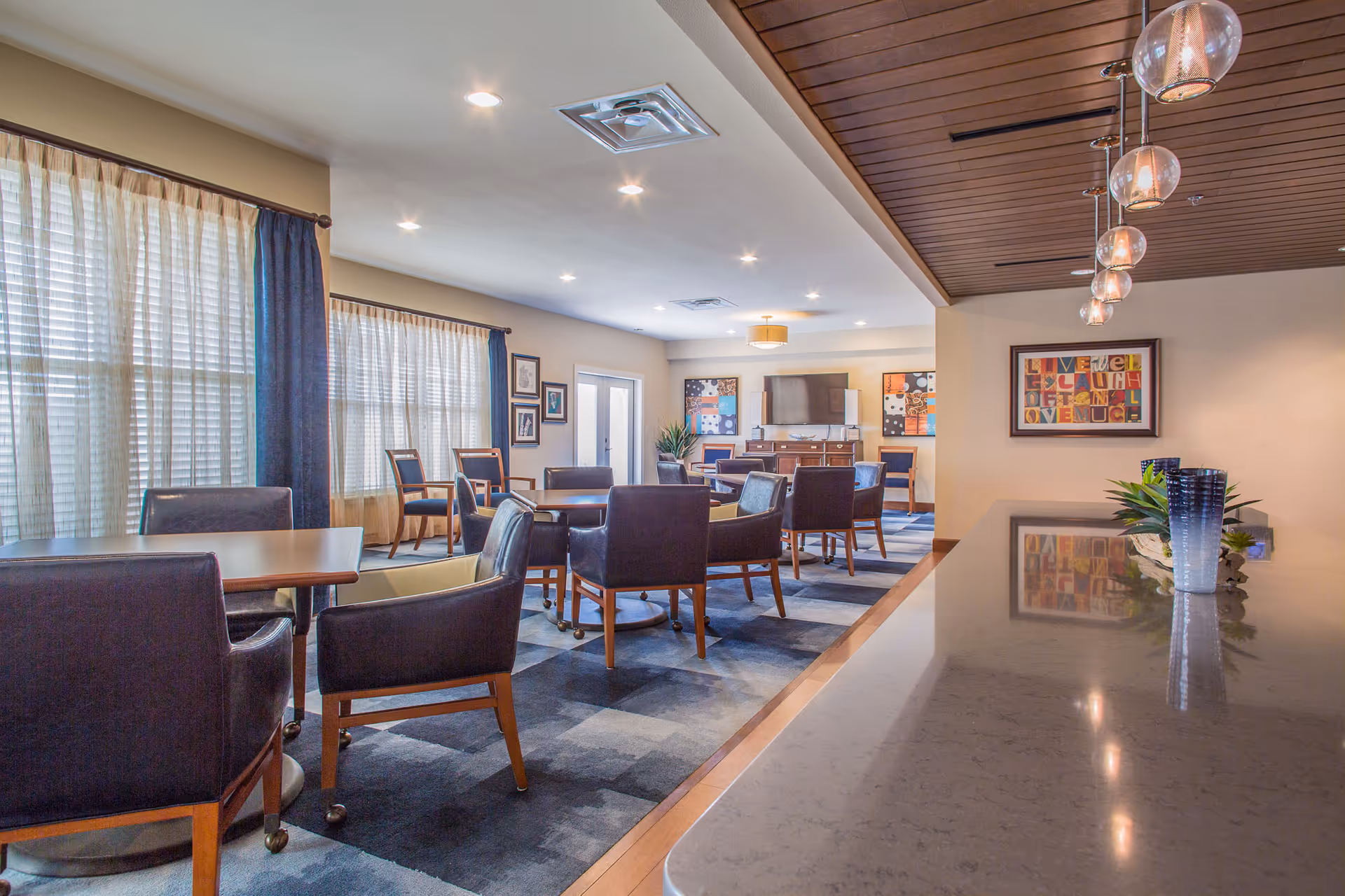 Bright communal lounge and dining area with tables and chairs, a TV console, and pendant lights.