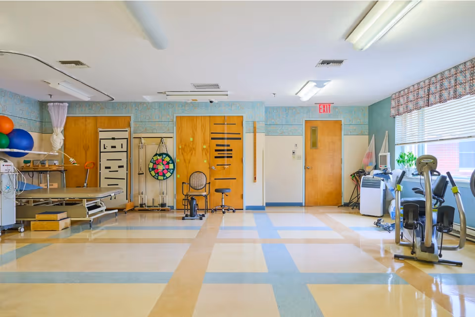 Bright rehabilitation and exercise room with therapy equipment, exercise bikes, a treatment table, and colorful therapy balls.