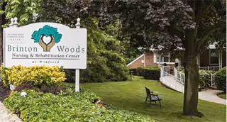 Sign for Brinton Woods Health & Rehabilitation Center at Winfield, with greenery near the building entrance.