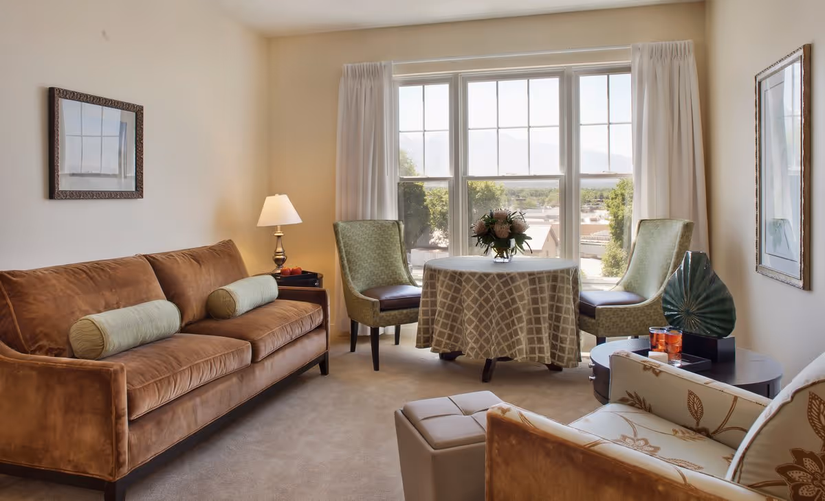 Bright living room with a brown sofa, two chairs and a small round table in front of a large window.