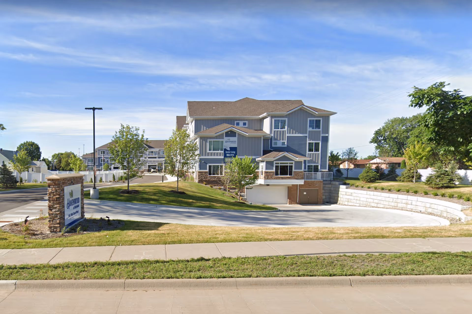 Front exterior of a multi-story senior living building with a circular driveway, landscaped lawn, and a stone entrance sign for Havenwood of Richfield.