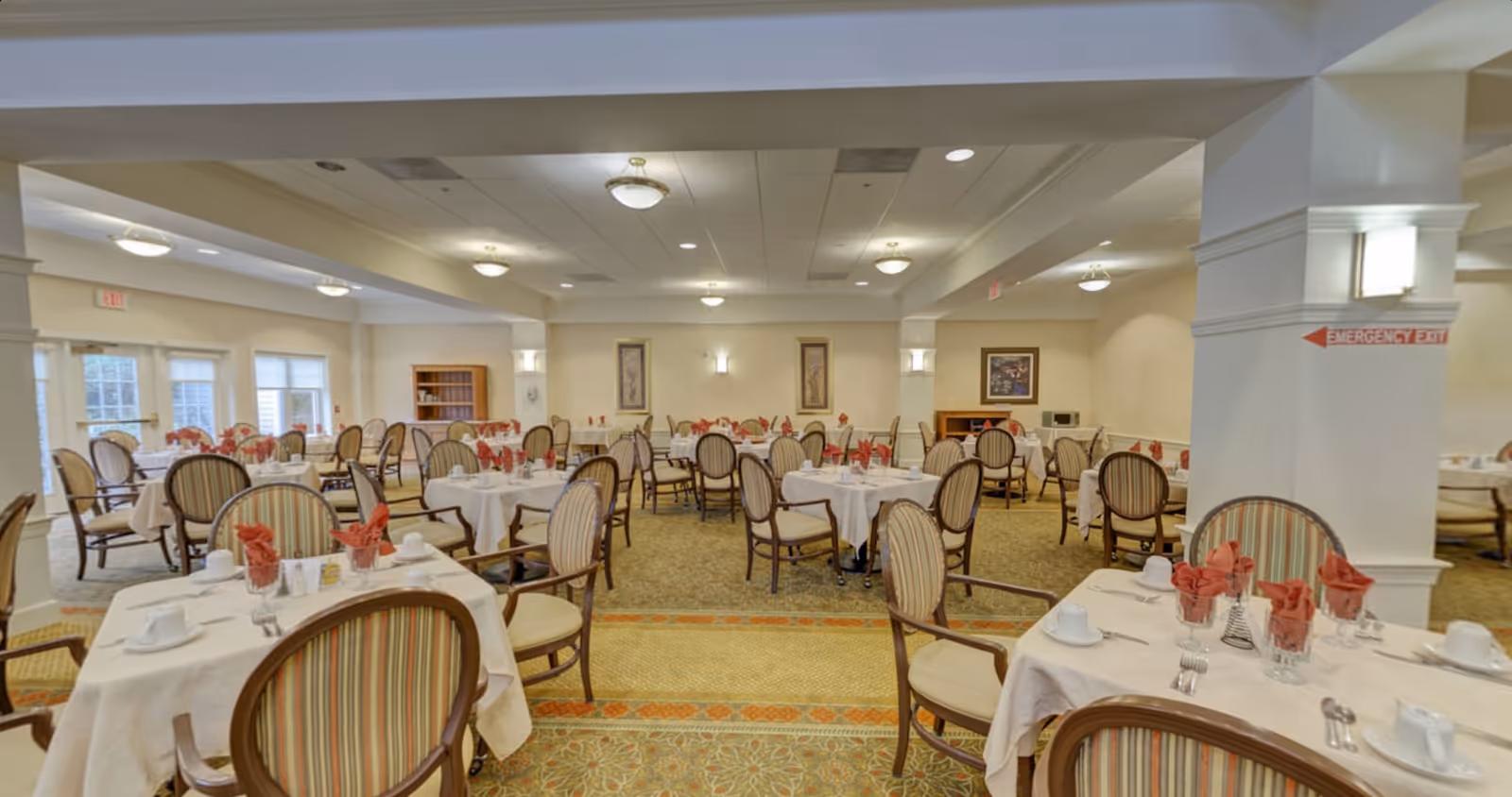 Spacious dining room with round tables set with white linens, striped cushioned chairs, and folded red napkins.