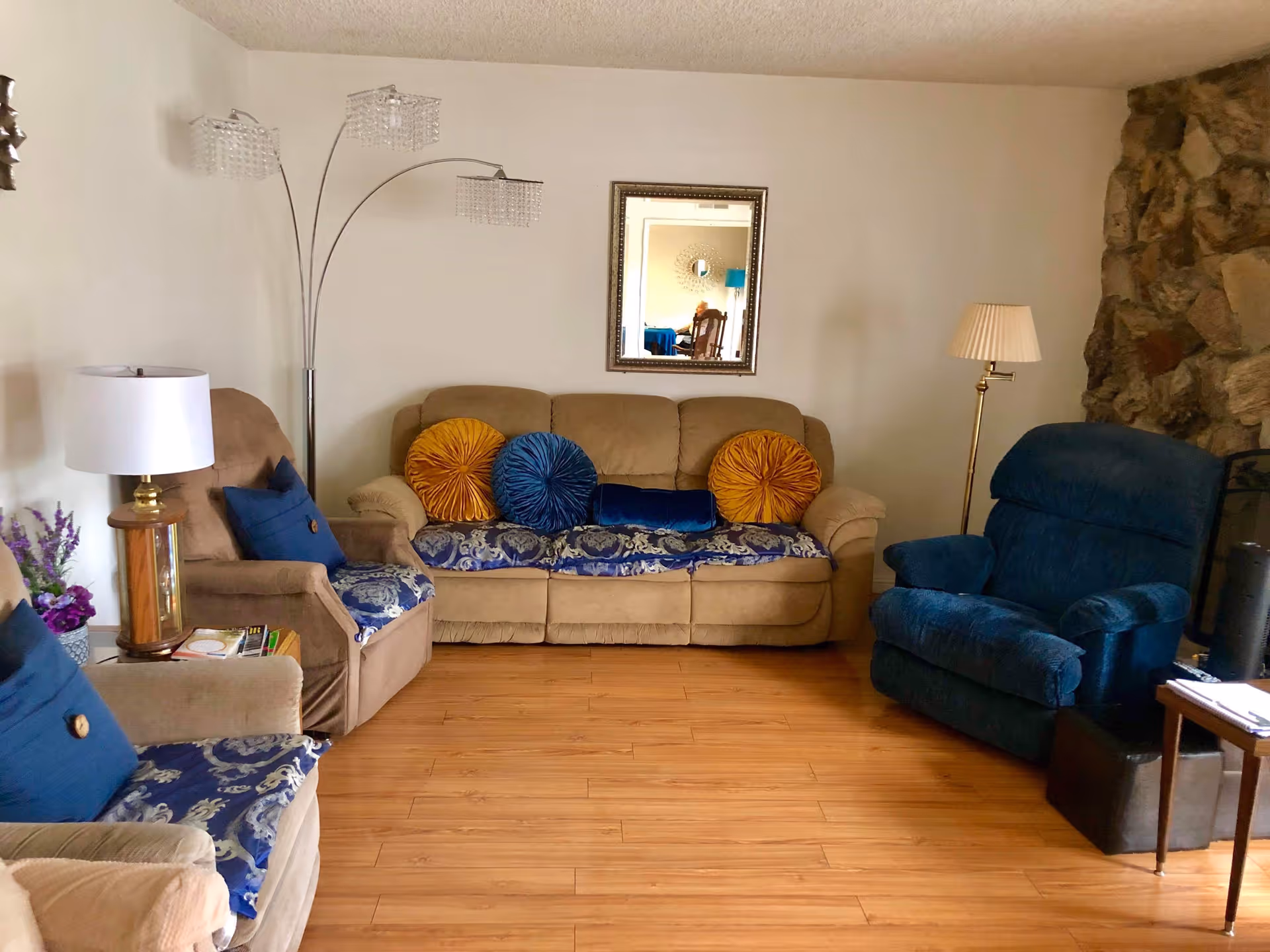 Comfortable living room with a beige sofa, blue recliner and armchairs, decorative pillows, lamps and wood flooring.