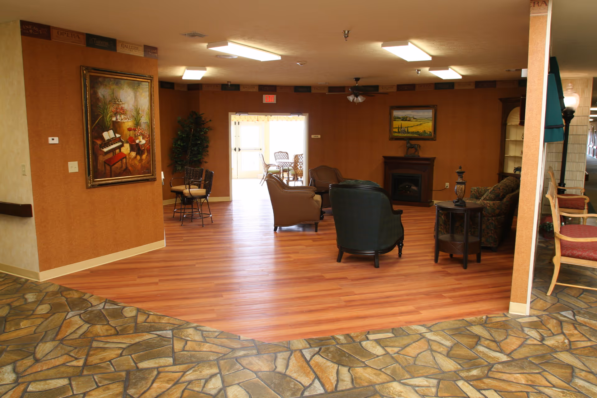 Communal lounge area with seating, tables, artwork, and mixed tile and wood flooring.