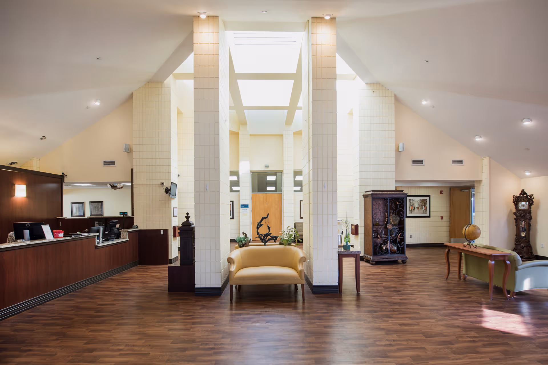 Spacious senior living facility lobby with a reception desk, central seating, and decorative furniture under a high ceiling.