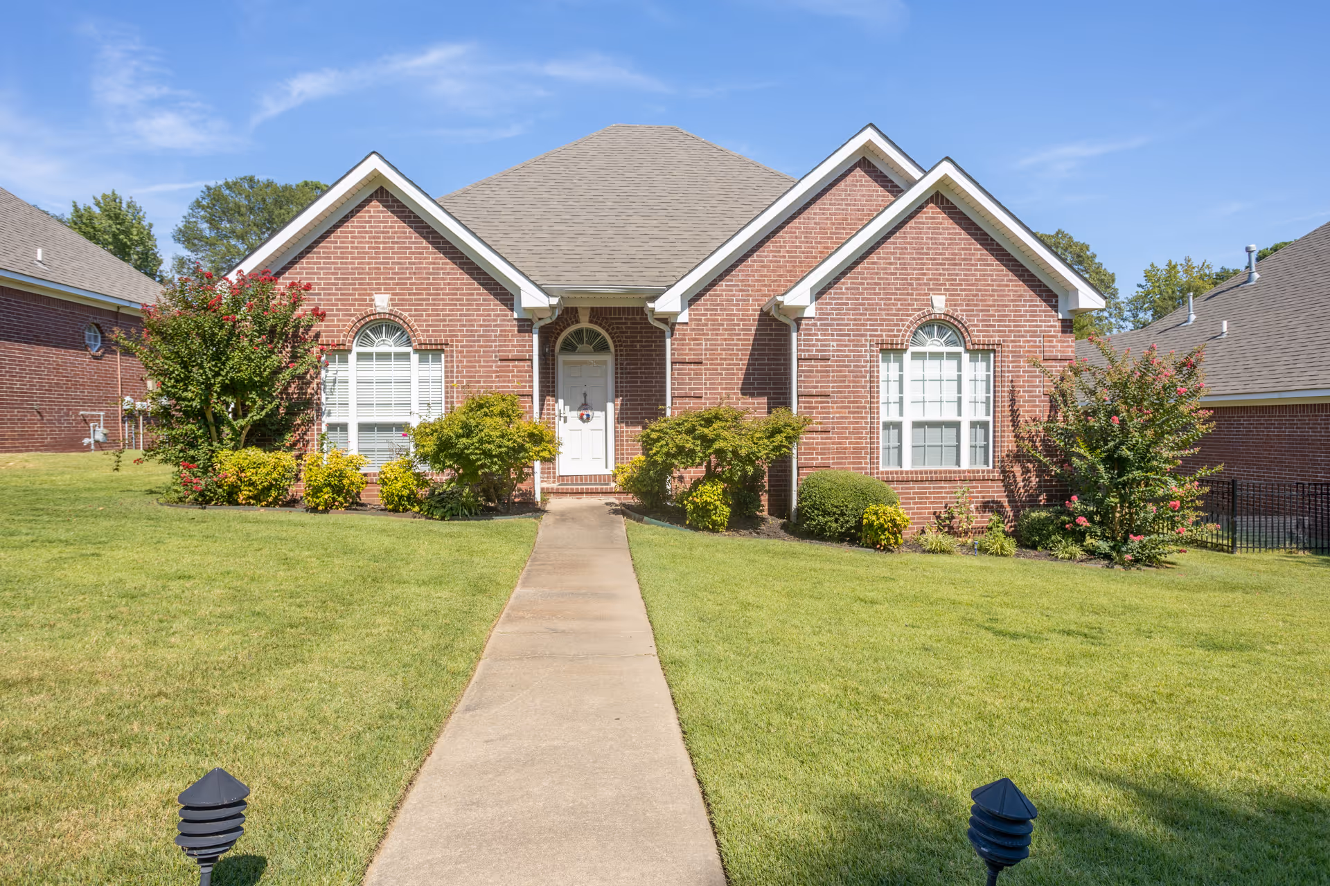 Front view of a single-story brick house with a central walkway, arched windows, and a manicured lawn.
