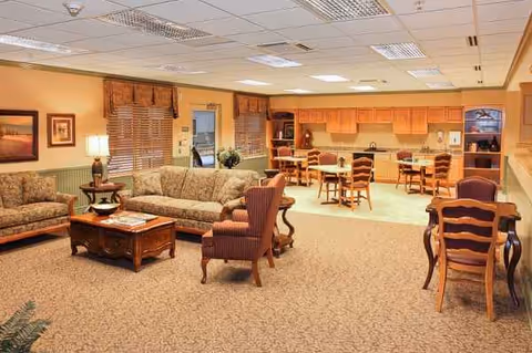 Spacious senior living lounge with sofas, chairs, coffee tables, and an open dining/kitchen area.