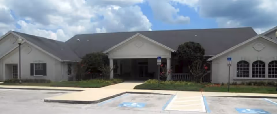 Front exterior view of a single-story building with a covered entrance, surrounded by landscaping and handicap parking spaces in front under a partly cloudy sky.