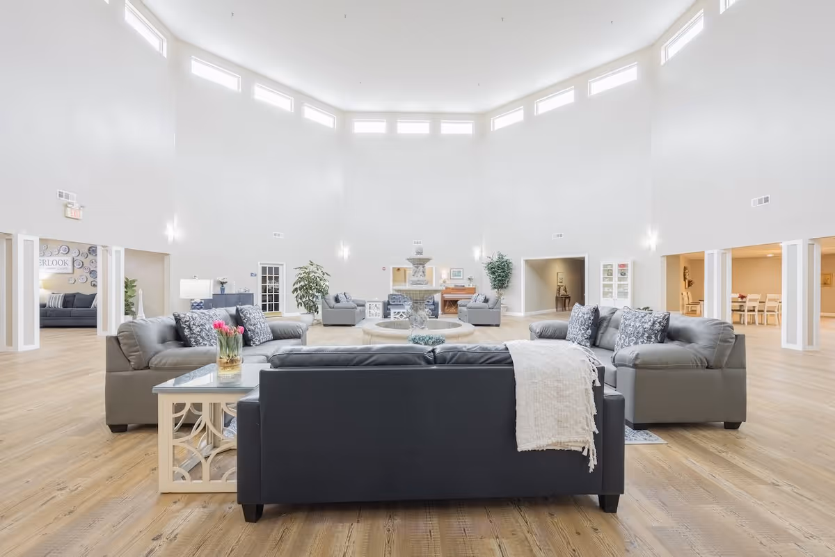 Bright, open communal lounge with sofas arranged around a central fountain under tall windows and high walls.