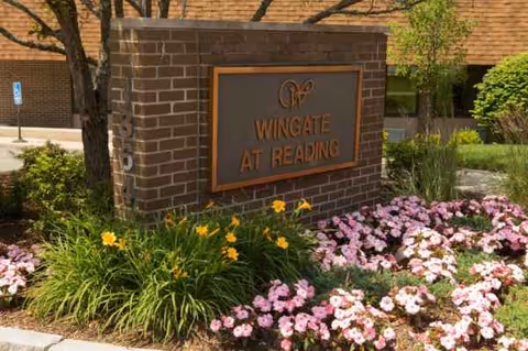 Brick entrance sign for Wingate at Reading, framed by blooming flowers and greenery.