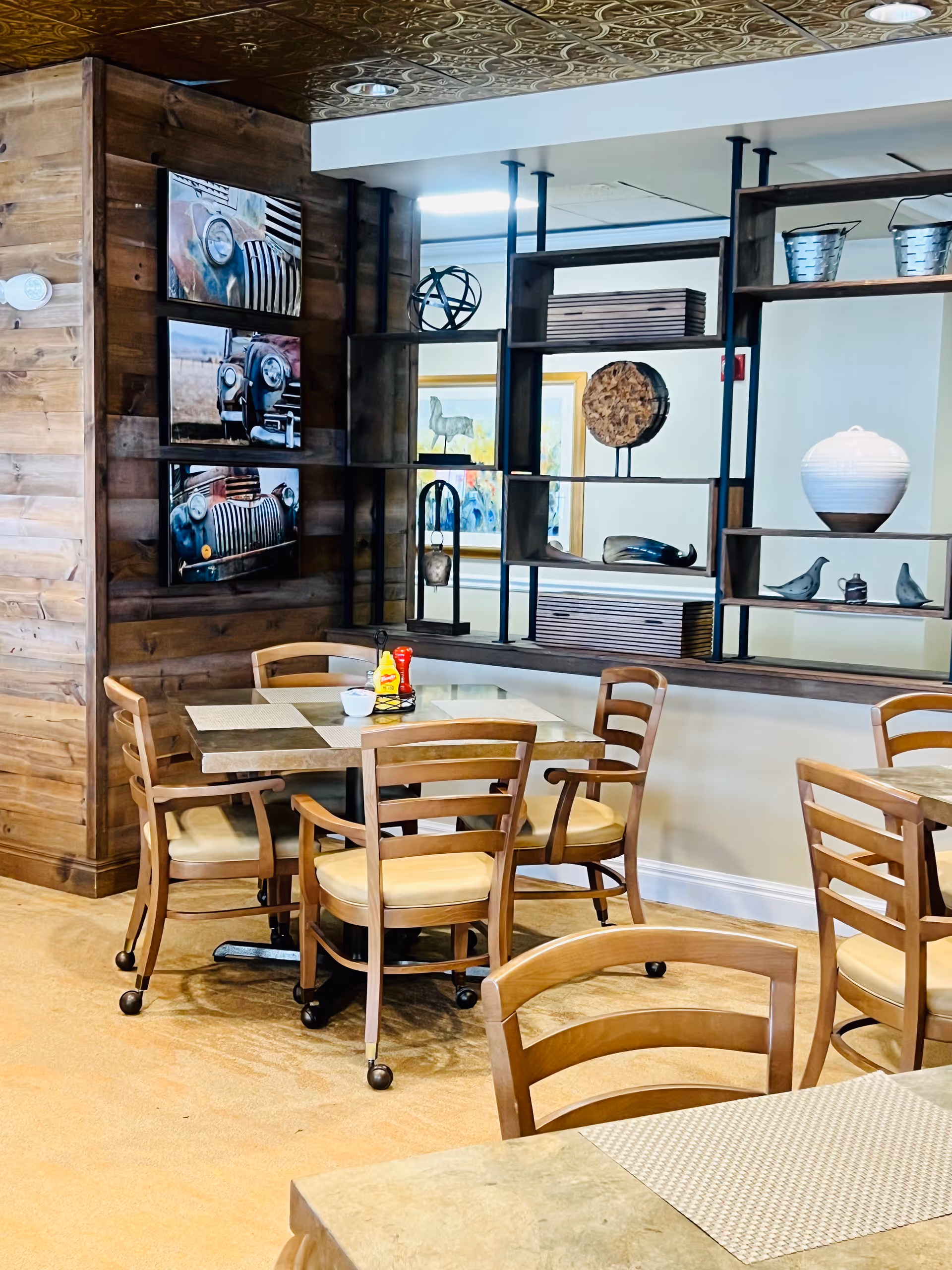 Indoor dining area with wooden tables and chairs, decorative shelving, and framed wall art.