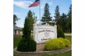 Outdoor view of a sign for Riceville Family Care and Therapy Center surrounded by landscaping with bushes and trees, with an American flag flying on a flagpole in the background.