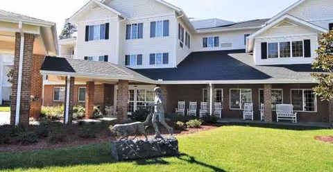 Exterior view of Holiday Cedar Ridge senior living facility with lawn, porch seating, and statue.