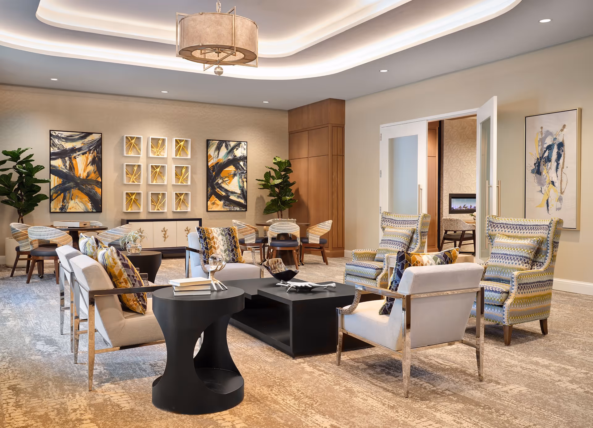 Bright, stylish communal lounge with armchairs and sofas arranged around coffee tables, abstract wall art, and potted plants.