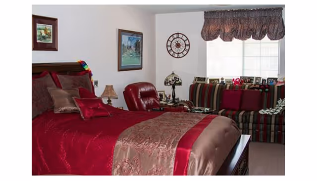 Bedroom with a red and brown bedspread, a leather recliner, and a striped sofa beneath a window.