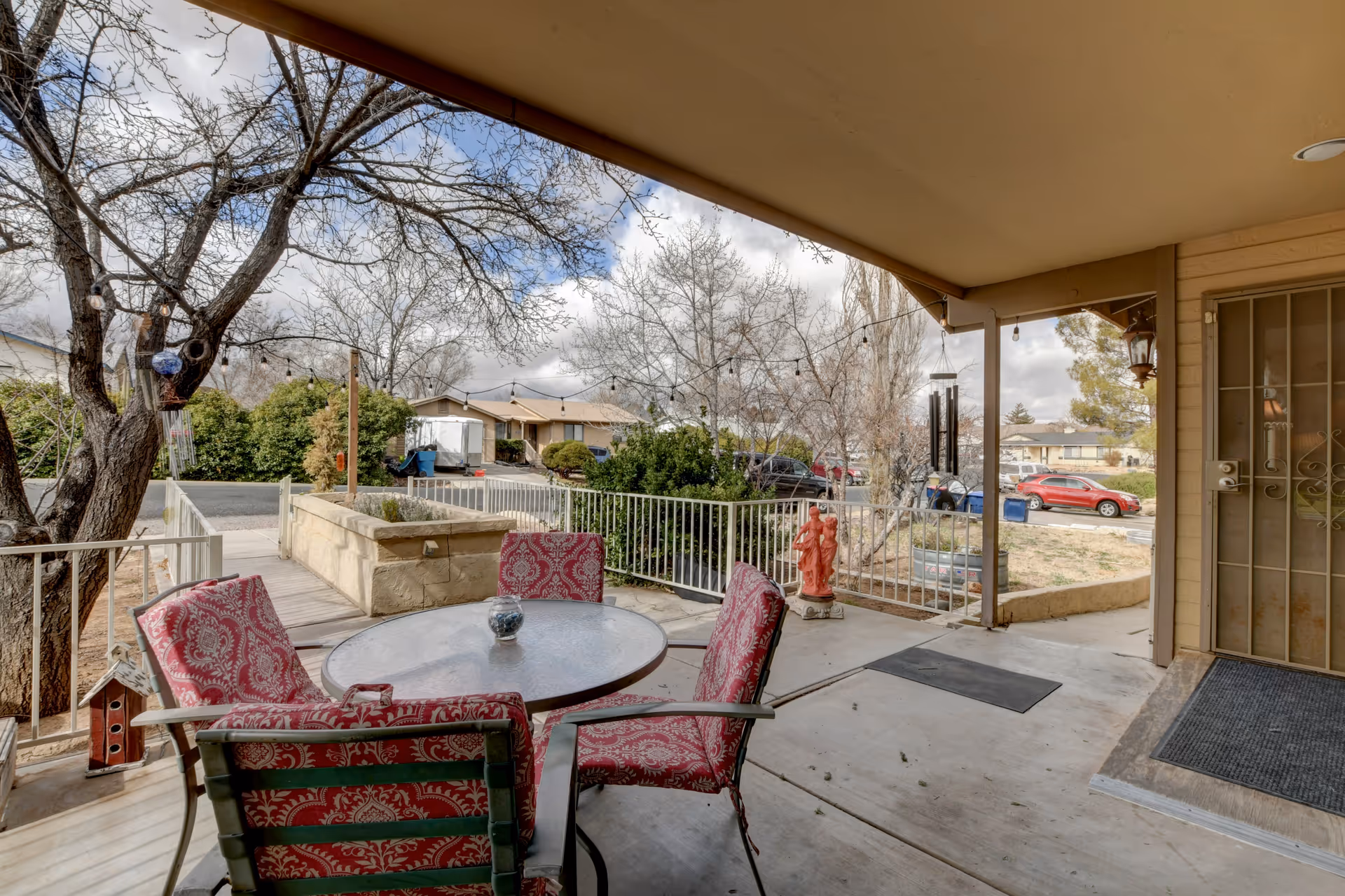 Covered front porch with a round glass table and red patterned chairs overlooking a residential street.