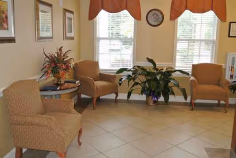 Bright lobby seating area with beige chairs, plants, and windows.