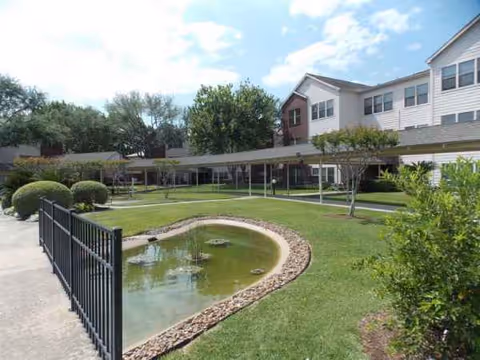 Exterior view of Lone Star Living campus with lawn, pond, and covered walkway.