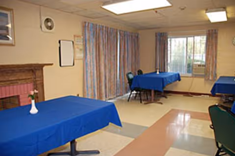 Communal dining room with blue-covered tables, chairs, and curtains in a senior facility.