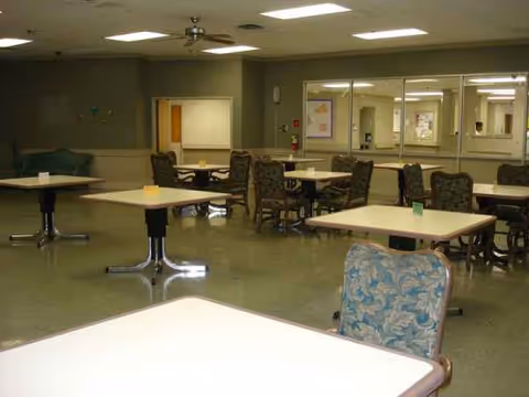 Empty senior living facility dining room with multiple tables and patterned chairs.