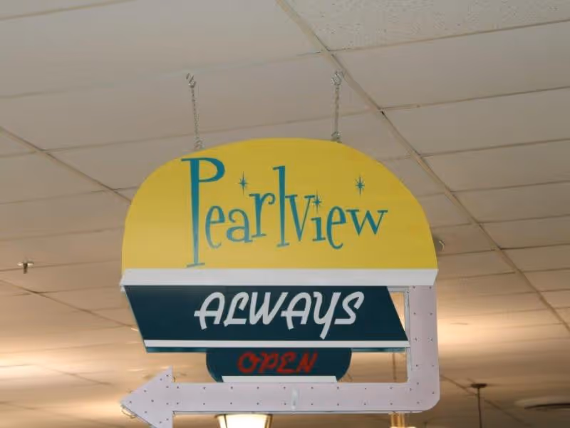 Hanging indoor sign that reads 'Pearlview ALWAYS OPEN' with an arrow beneath a drop ceiling.